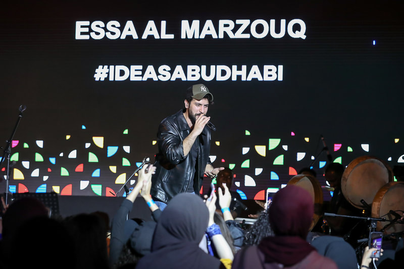 A picture of Essa Al Marzouq performing on stage, with members of the crowd taking photos of him.
