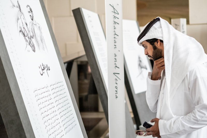 Image of a man in Arabic national dress looking at a poem written in arabic